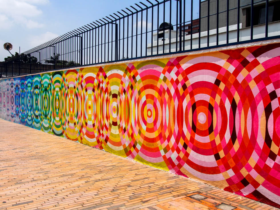 A mural in Bogota, Colombia with a rainbow of colors painted on a low wall