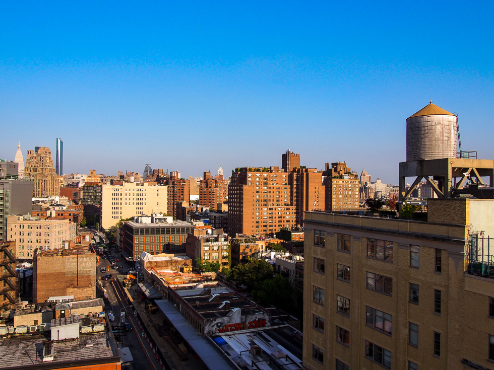 View from the Whitney Museum in Manhattan, New York during the golden hour, with brown and orange buildings in NYC and a water tower in the foreground
