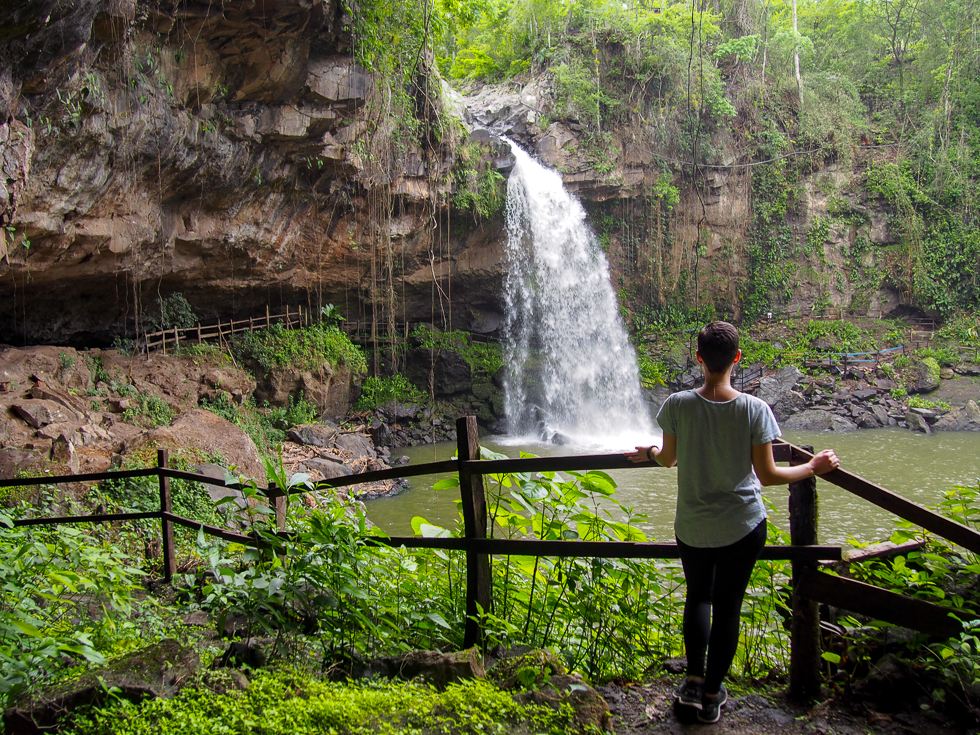 Solo female travel in Nicaragua: Alissa stands with her back to the camera, looking out over Nicaragua's Cascada Blanca, a waterfall surrounded by a half-cave and much greenery