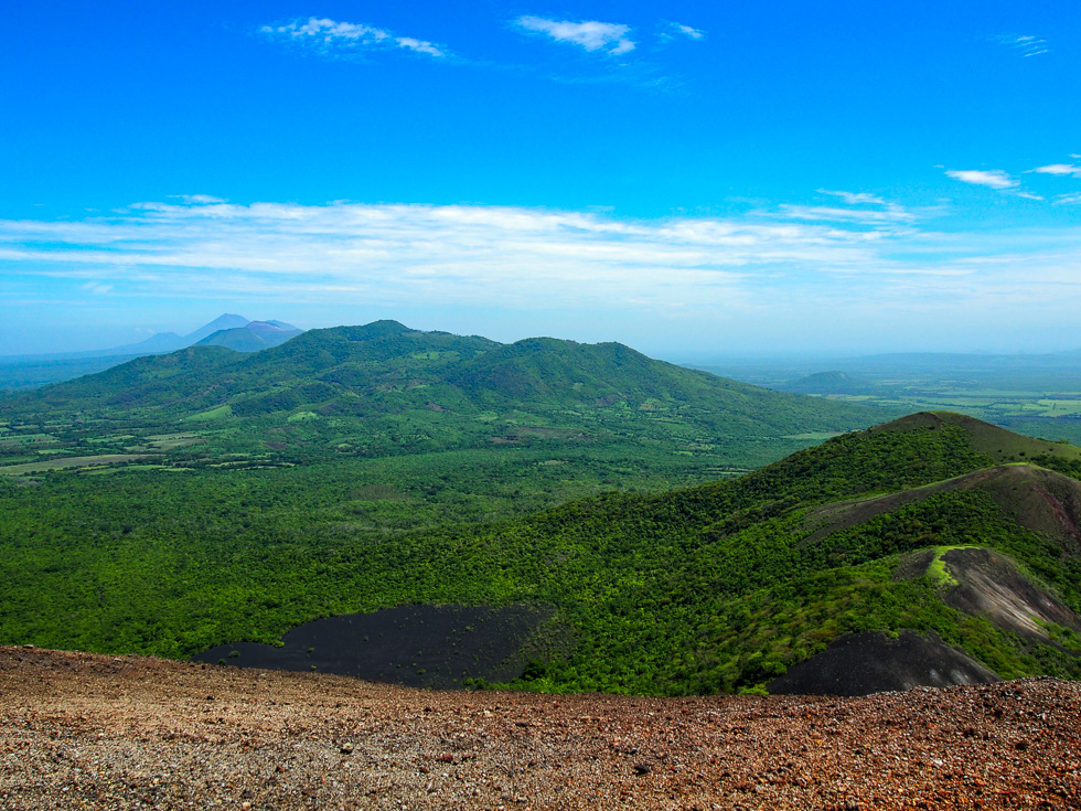 View of a range of volcanos in Nicaragua, seen from the Cerro Negro volcano, under a blue sky.