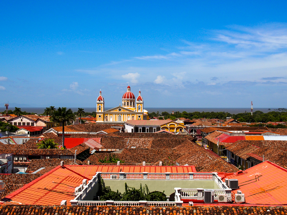 View of Granada, Nicaragua, including the red rooftops of building across the city, the cathedral, and Lake Nicaragua in the background on a sunny day.