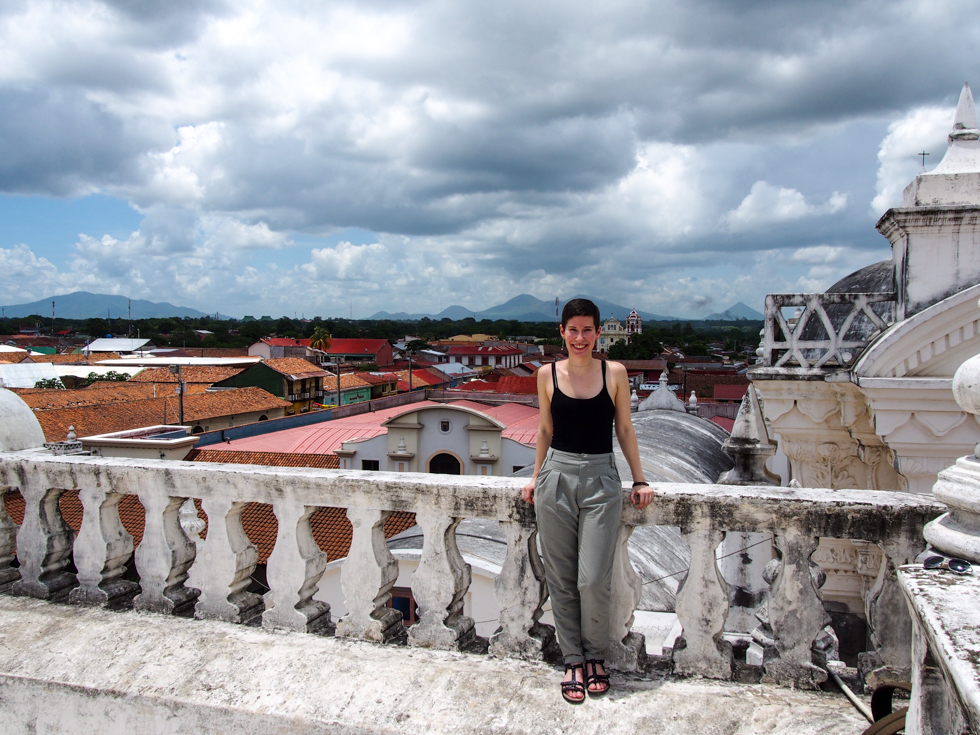 Solo female travel in Nicaragua: Alissa on the rooftop of the cathedral in Leon, smiling in the sunshine, with a backdrop of the city and various volcanoes behind her