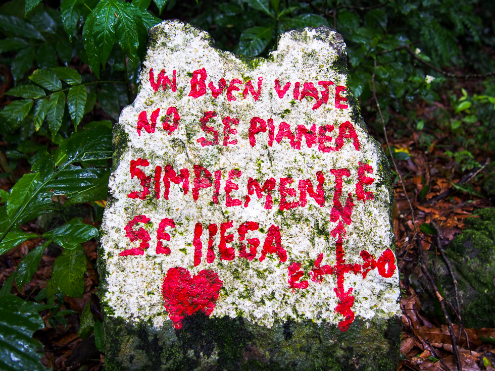 Painted rock seen on a wet hiking trail in the Selva Negra cloud forest, reading "un buen viaje no se planea, simplemente se llega" (a good trip is not planned, it simply arrives) in pink letters