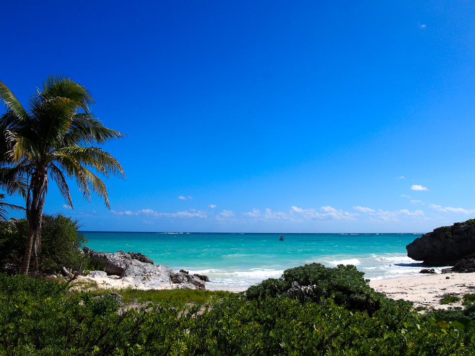Beach in Tulum, Mexico on a sunny day, with white sands, clear blue water and a blue sky