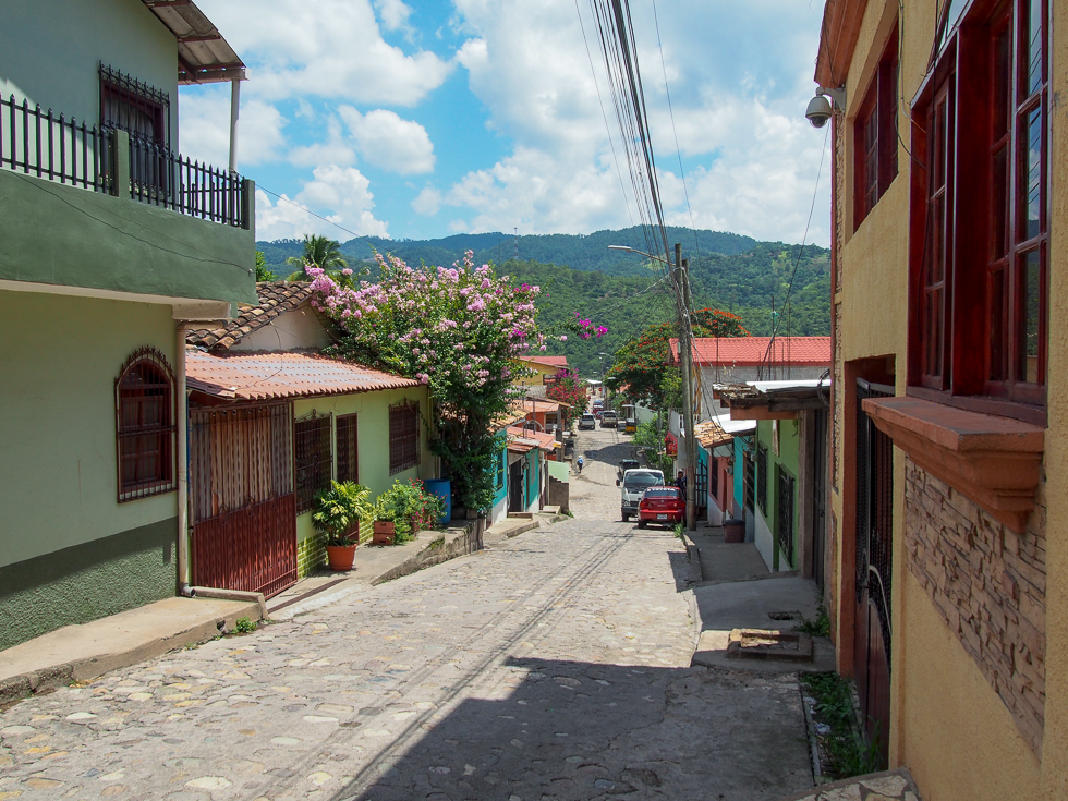 A street in Copan Ruinas, Honduras, with colorful homes on either side and a view of the mountains in the distance
