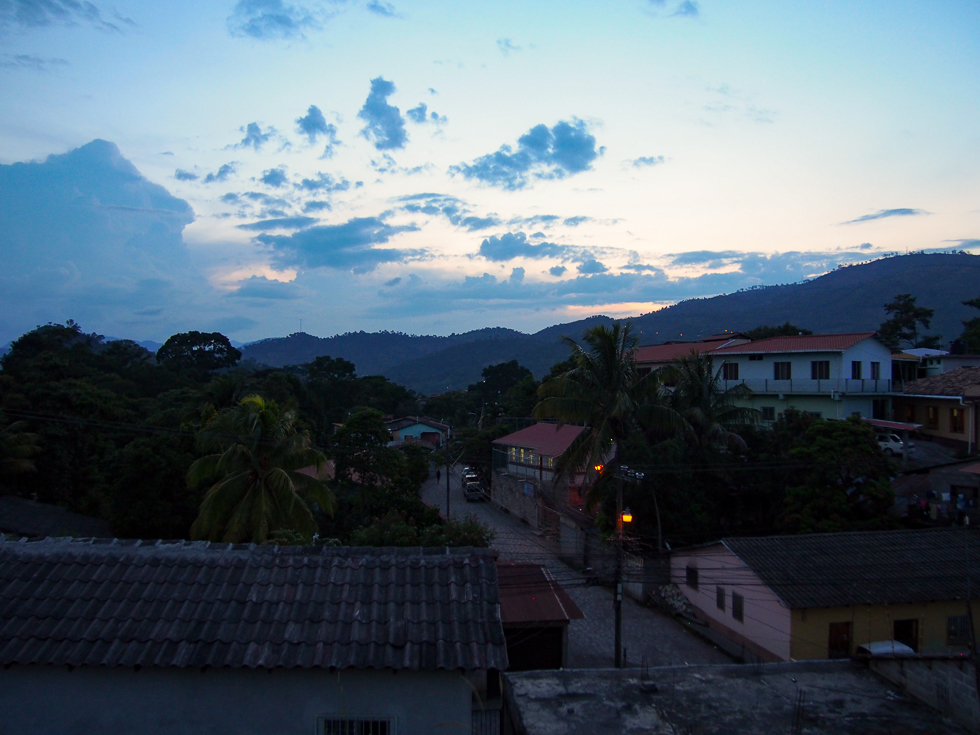 A dark shot of Copan Ruinas, Honduras, in which the sun has already set over the mountains in the distance and day is turning to night