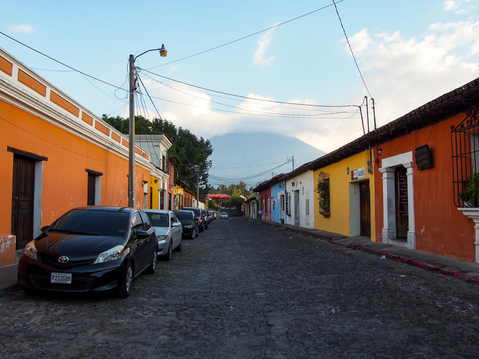 A typical street in Antigua, Guatemala: cobblestones surrounded by colorful homes on both sides, with the Water Volcano in the distance